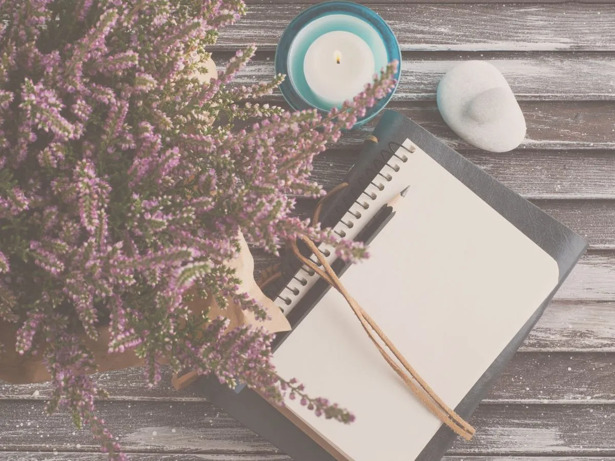journal on a desk with a pencil, candle, stones, and a lavender plant